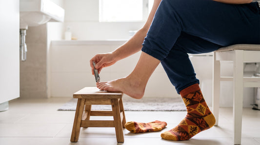 Person trimming toenails straight across in a bright bathroom, autumn socks and boots nearby